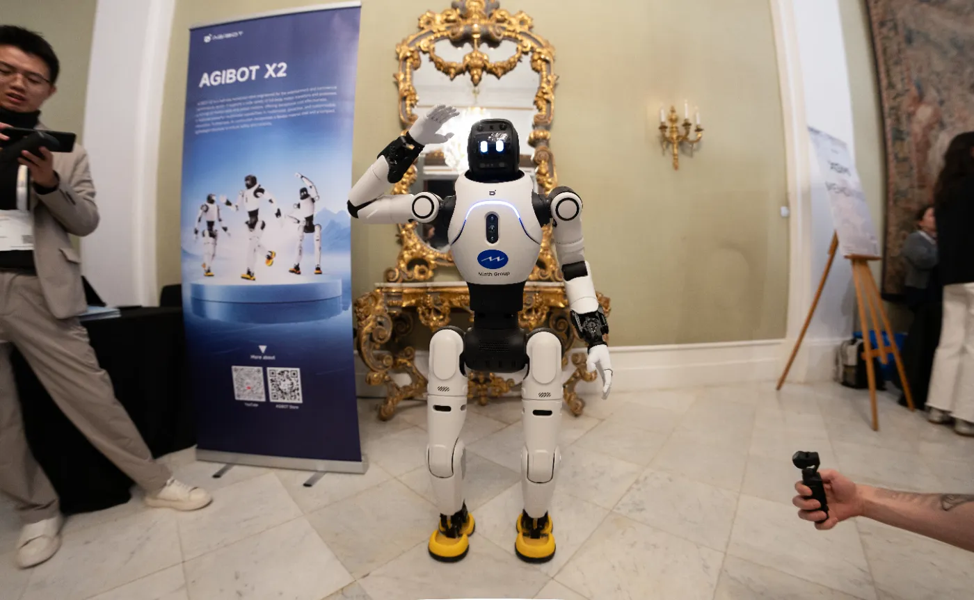 Le robot humanoïde AgiBot X2 salue le public, entre une affiche de présentation et des visiteurs, sur un salon